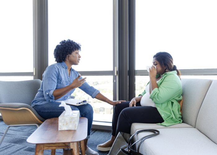 Meeting with her therapist, the young adult pregnant female wipes tears from her eyes as she talks about her fears.