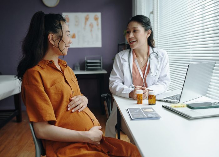 Smiling pregnant woman talking to attentive female doctor at clinic during prenatal checkup, discussing health and wellness strategies together