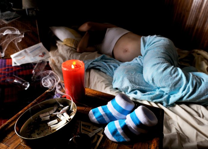 a smoking and drinking pregnant immigrant woman lying in bed, expecting a baby boy in the coming days.