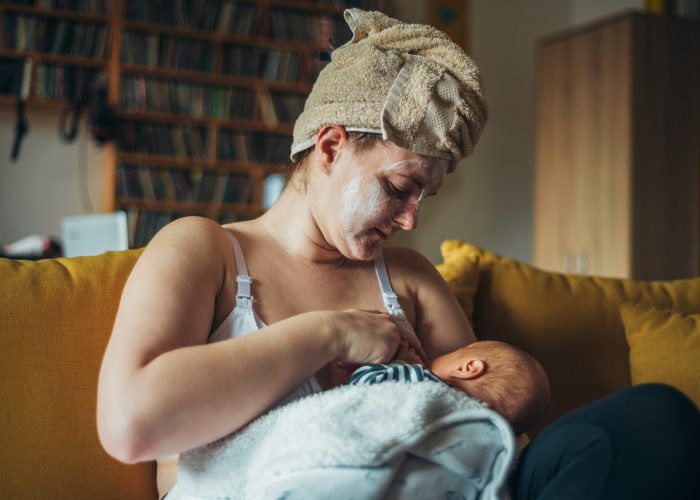 Shot of a mother breastfeeding her baby boy while wearing a spa face mask and a towel on her head